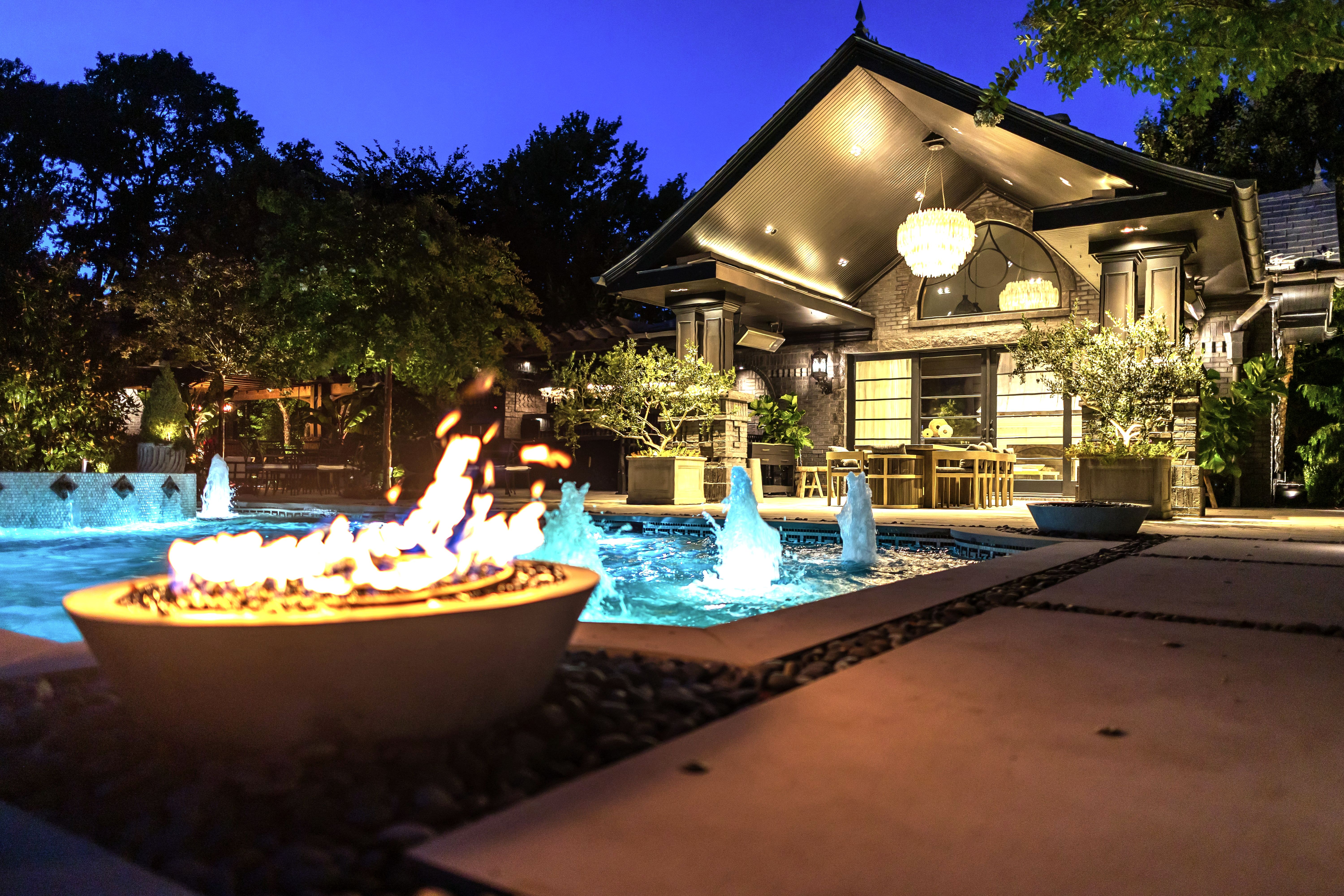 Night pool with fire bowl, fountains and lit pavilion